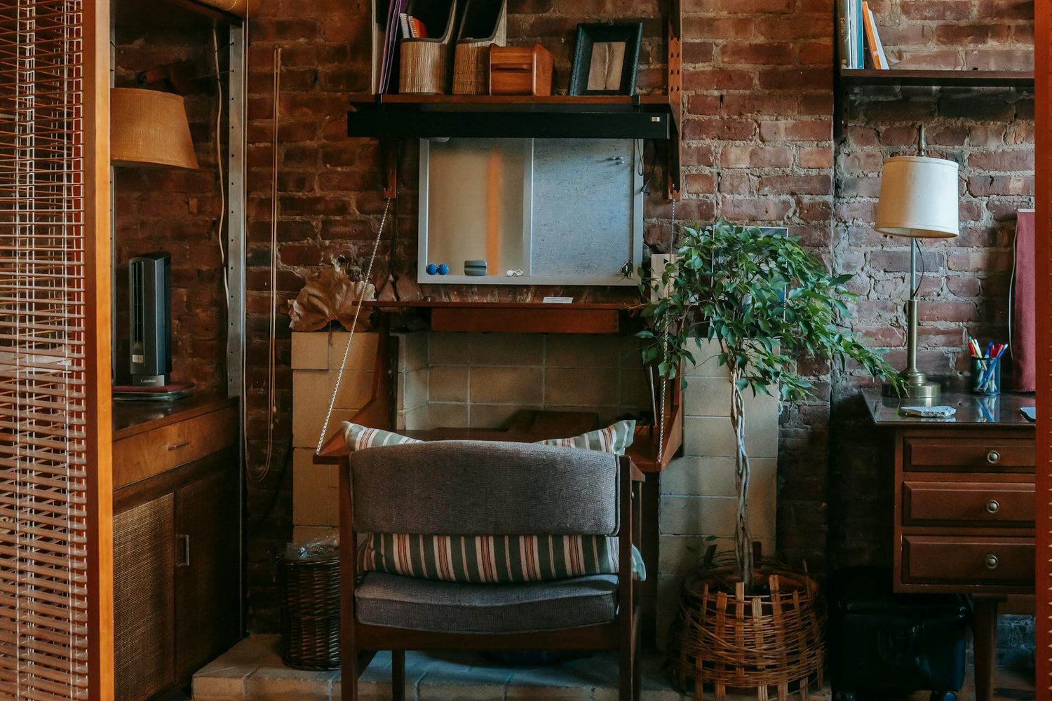 Small space urban living room with brick wall, chair, and small table with lamp and plant.